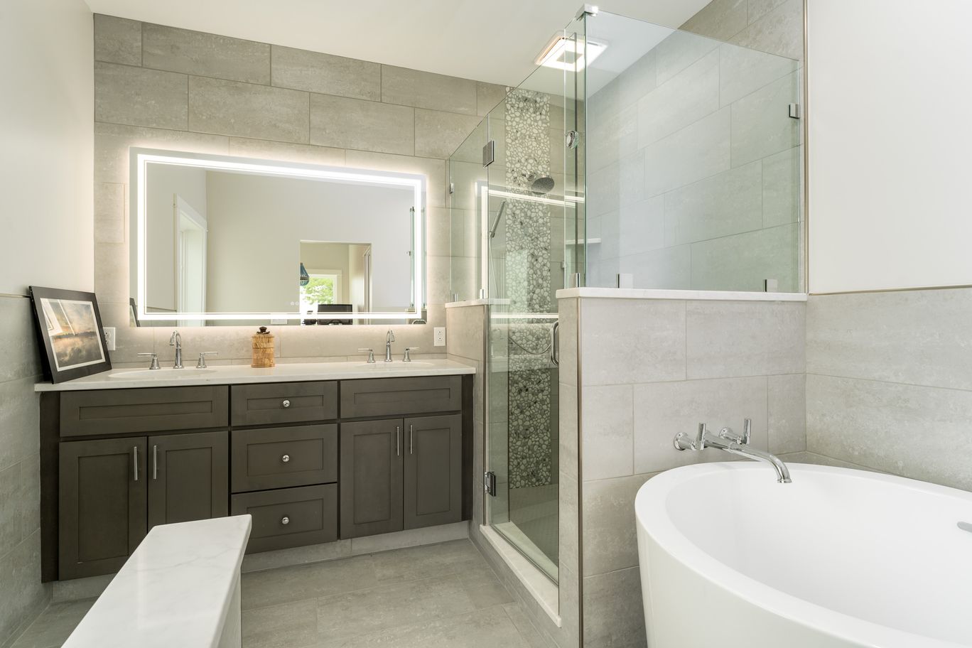 Bathroom with a freestanding tub, a glass shower, and a backlit mirror.