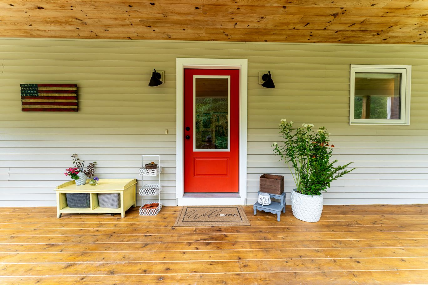 Front porch with a red door on sage siding under a pine ceiling.